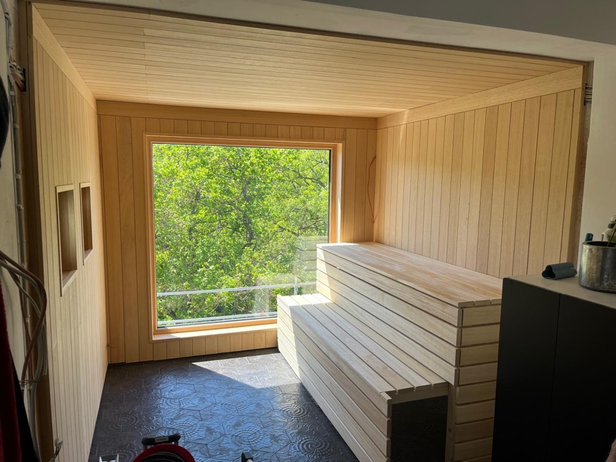 Fertig gebaute Sauna aus hellem Holz mit Panoramafenster ins Grüne